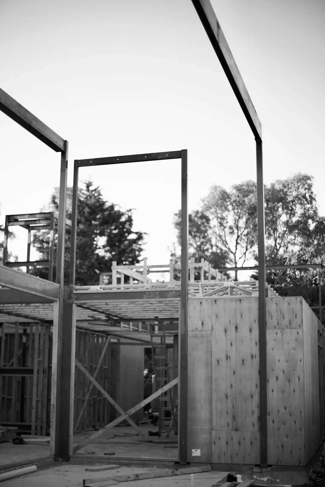 Steel portal frames rising above a timber-framed house under construction